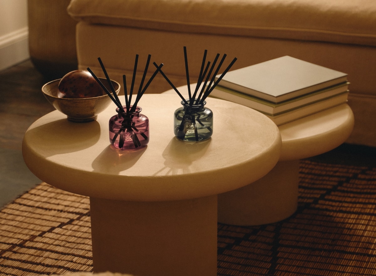 A pair of colourful refillable diffusers on a round table, styled with books and décor in a warm, neutral living room setting.